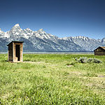 Wooden outhouse and barn are part of a series of structures in a historic settlement called Mormon Row. This settlement is near the base of the Grand Tetons.