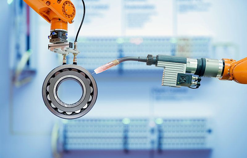 Close-up of industrial robotic arm gripping a spherical roller bearing in a welding operation.