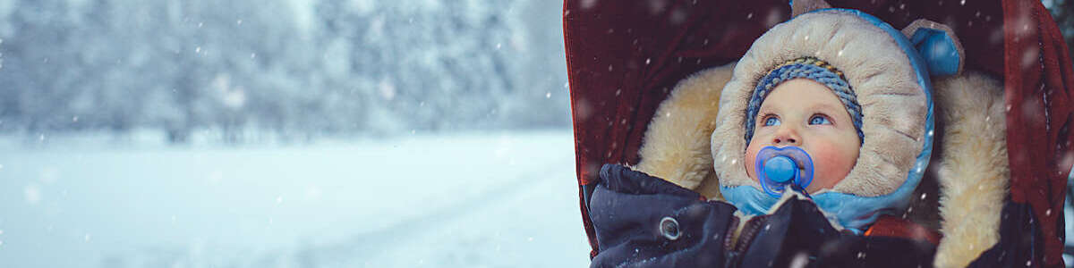 Baby boy in a stroller stares with bright blue eyes into a snowy winter landscape.