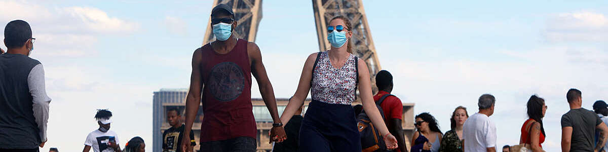 Couple wearing a protective mask walk a front the Eiffel Tower in France.